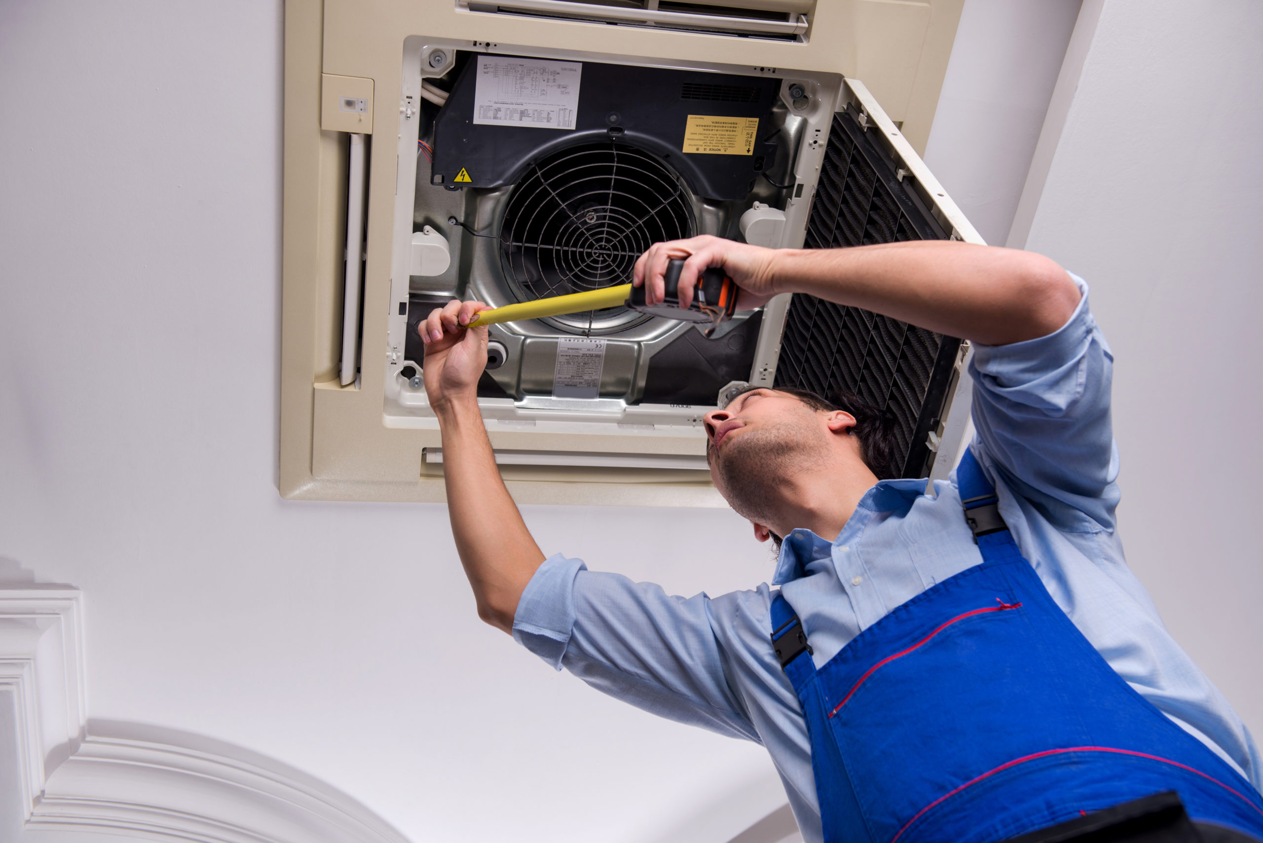 Person in blue overalls inspecting indoor AC unit with flashlight